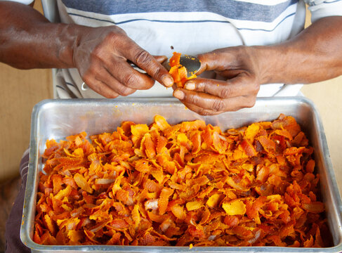 M&atilde;os de um homem raspando com uma colher o fruto buriti sob uma forma de alum&iacute;nio. 