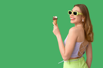 Happy smiling young woman holding ice cream in waffle cone on green background