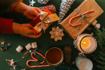 A child’s hands holding a festive red gift box with a golden ribbon bow, surrounded by Christmas...