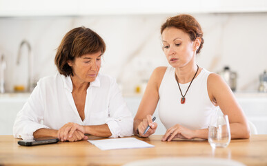 Fototapeta premium Two woman at table and trying to figure out finance problem and thinking about bills