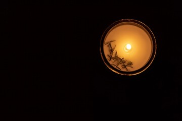 A glowing candle in a glass jar illuminated against a completely dark background