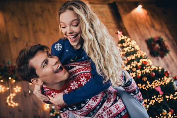 Photo of lovely young couple cheerful hug piggyback dressed christmas outfit day light home party decoration interior room