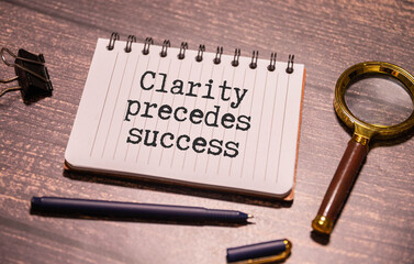 text Clarity precedes success on easel with office tools and paper.