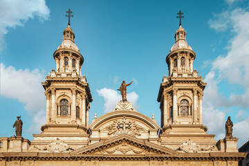 Obraz premium The upper section of the facade of the Metropolitan Cathedral of Santiago, Chile, featuring the twin bell towers and, amidst, the bronze statue of the Virgin Mary to whom the cathedral is dedicated.