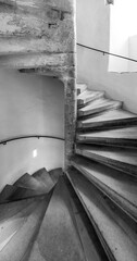 A spiral staircase ascends gently, revealing textured stone steps and a subtle play of light against the walls, creating an atmosphere of elegance and intrigue in a serene environment.