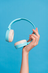 Cropped close up vertical photo of lady hand hold demonstrate wireless headphones isolated on blue...