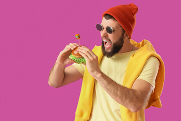 Young man eating tasty burger on pink background