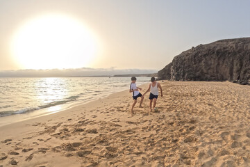 two young friends play football at sunset on a lonely beach with cliffs in the background on a summer day, holidays with family and friends, playing together