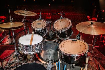 Obraz premium A complete drum set on stage with cymbals, snare, and toms, equipped with microphones, ready for a live music performance in an empty auditorium.