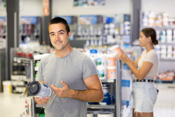 Guy examines can of paint and buys, collects necessary supplies in store according to list for...