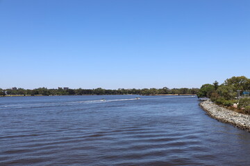wide-angle landscape panorama deep blue waters of a wide river and reinforced rocky bank in urban setting under cloudless deep blue skies