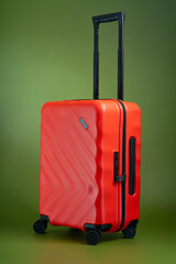 A tilted orange suitcase luggage isolated on olive green background