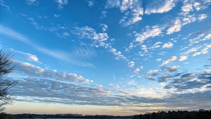 Obraz premium Gentle morning light dancing across a canvas of expansive blue sky with scattered wispy clouds, natural scenery, gentle breeze, cloudy skies, serene atmosphere