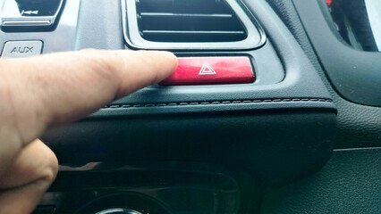 Man pushes a triangle emergency button on car dashboard. finger hitting car emergency light button,...