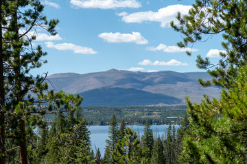 A serene view of a tranquil lake surrounded by evergreen trees and mountains under a clear blue sky in the daytime