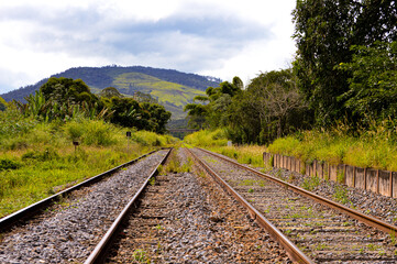 Fototapeta premium Railway tracks extending into the distance, surrounded by natural scenery. The focus highlights the metal rails and gravel bed, with parts of the background gently blurred for depth.