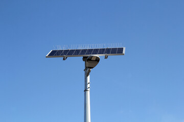 Solar-powered street light with bird spikes against a blue sky background