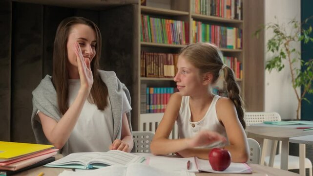Caucasian woman child little girl elementary school teacher tutor teamwork book textbook positive schoolgirl student lesson high five learning achievement exam female studying task together education