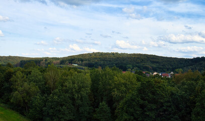 Fototapeta premium Sun shining on hills with green trees and houses on a summer afternoon in Germany.