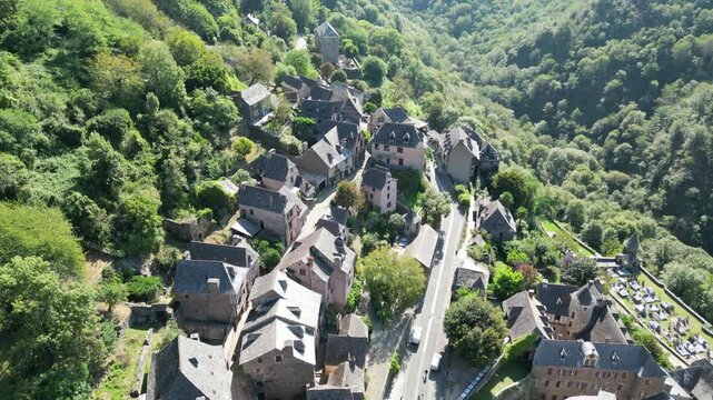 Drone aerial view in France countryside small old medieval town and a cathedral surrounded by a green mountain forest flying over in Conques