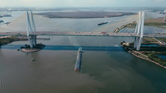 Two huge ships leaving the port of Houston going under Fred Hartman Bridge while cars drive on it.