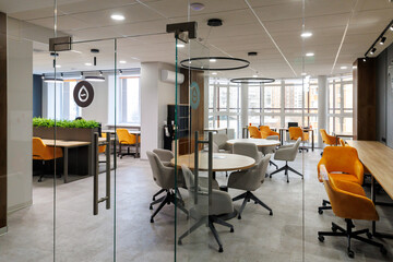 modern office space featuring office interior glass wall, with views of round grey desks and yellow chairs. bright environment is enhanced by natural light streaming through large windows