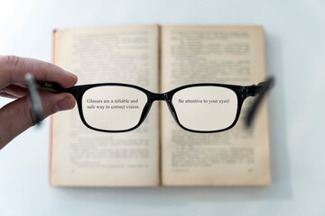 book and eye glasses for read and write over blurred background with copy space, reading glasses in his hands on a blurry book background. poor vision concept.