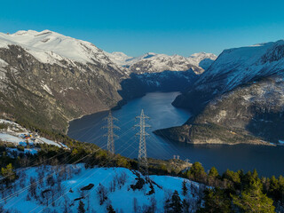 High voltage line over the mountain. With fantastic nature in the background. Snow covered mountains with the fjord below. Norway.