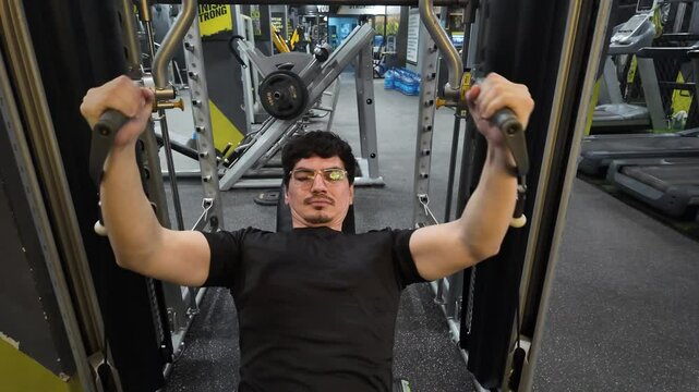 Close-Up View of Handsome, Well-Toned Man Wearing Glasses Performing Cable Incline Fly for Chest Development, Demonstrating Fitness Dedication on an Incline Bench with Cable Fly Machine in Gym