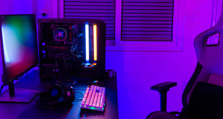 A computer setup with a purple light dark background, games transmission modern equipment, modern gaming PC on desk with keyboard mouse monitor, gamer work space concept © sorapop