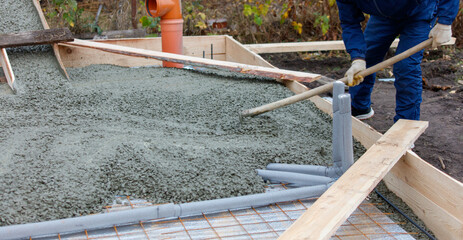 A man is laying concrete on a wooden board