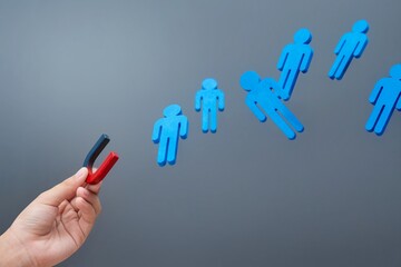A hand holding a magnet attracts blue wooden figures. Attraction concept.