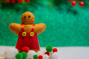 Ginger cookie doll with snow balls on shimmering green color and Chirstmas ormament blackground.