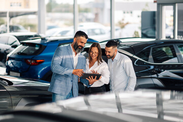 Car dealership staff collaborate on a tablet among new vehicles.