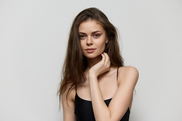 Fototapeta premium Confident young woman with long hair wearing a black tank top, posing thoughtfully against a neutral gray background. Beauty and self-expression concept.