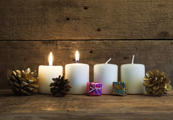 White Advent candles on a rustic wooden background, second candle is burning