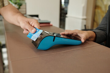 Hand holding credit card making payment on modern digital payment terminal with another hand...