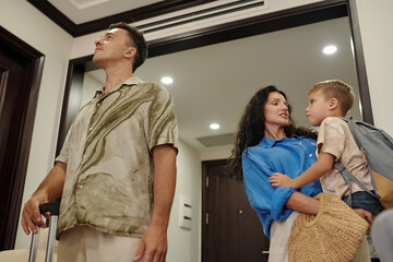 Naklejka premium Family entering home with packed belongings, child being held by mother while father looks around Room exudes warmth with a blend of modern and homely atmosphere