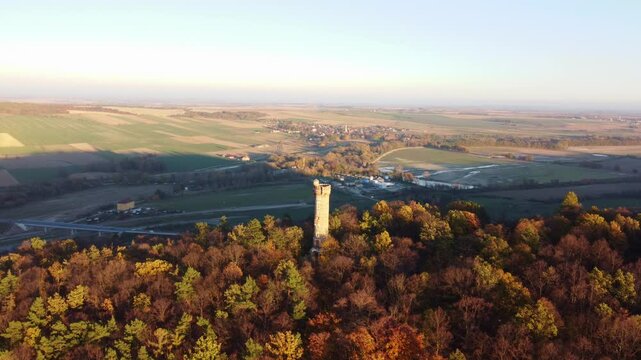 Aerial descend to Cvil&iacute;n lookout tower in Krnov, Czech Republic, surrounded by vibrant autumn trees at sunset