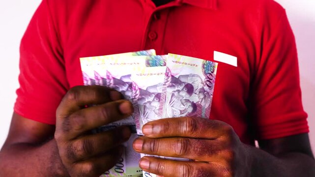  Black African man wearing red Polo shirt counting Botswana Pula notes over white background.