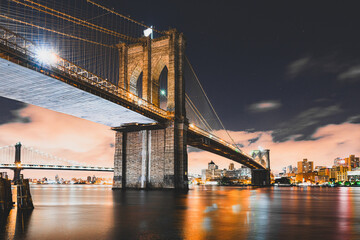 Fototapeta premium A long exposure of the Brooklyn bridge and Manhattan bridge with downtown Brooklyn in the background, over the East river with fast moving night clouds.