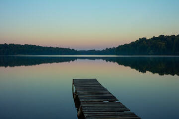 Obraz premium Wooden Pier Over Tranquil Lake at Dawn with Rainbow-Hued Sky Reflection