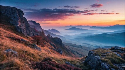 The soft glow of sunrise bathes the rugged landscape in warm hues contrasting with the cool colors of the descending fog.