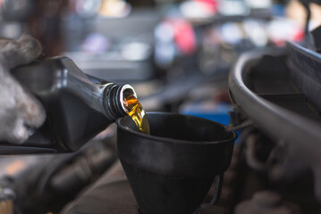 Close-up of motor oil being poured into a funnel during vehicle maintenance in an automotive workshop. Focus on precision.