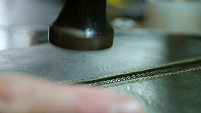 Tapping thread seam around zip-line with small mallet in shop closeup. Leveling zipper place on leather wallet side in craft atelier. Traditional work