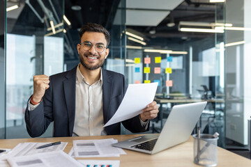 Businessman celebrates success holding documents. Confident professional in office setting, showing...