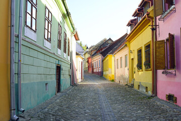 Obraz premium A street in the UNESCO World Heritage Site of Sighisoara's Old Town: old houses painted in different colours and a cobblestone road going up. A journey through the beautiful places of Transylvania