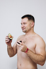 A man without a t-shirt holds an avacado and is satisfied