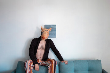 man in rubber pig mask sittihg on sofa
