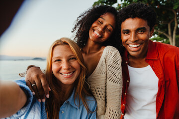 Friends taking a joyful summer selfie by the seaside at sunset